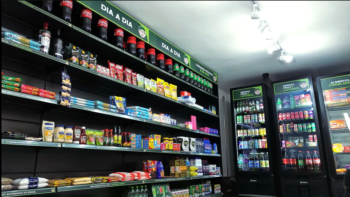 Interior de uma loja do Seo Juca com gôndolas abastecidas e geladeiras de bebidas ao fundo